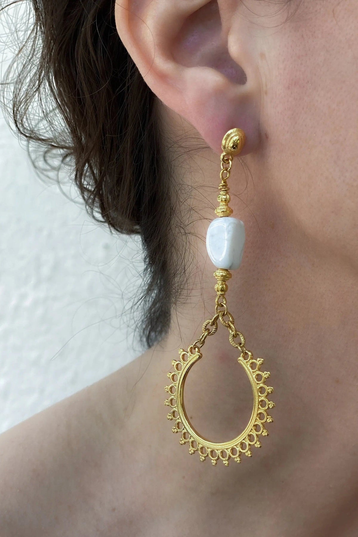 ÉRIS EARRINGS are gold-tone dangling earrings with a white stone and an ornate teardrop hoop detail