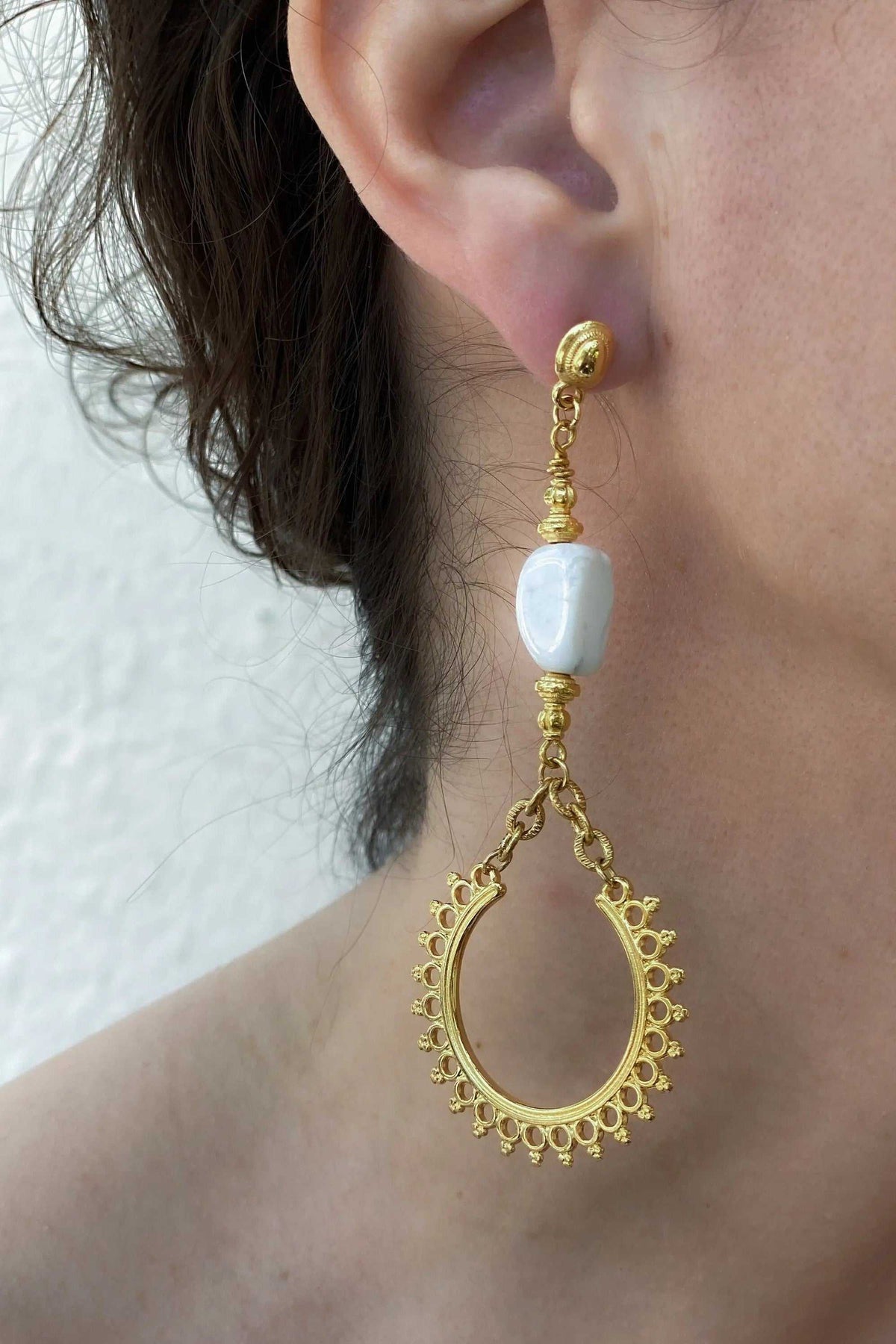 ÉRIS EARRINGS are gold-tone dangling statement earrings with a white stone bead and ornate open teardrop hoops