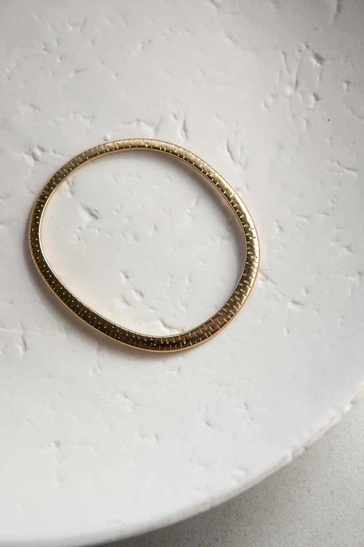 Ethnic Oval bangle in gold-tone metal, a thin flat oval bracelet with a textured, patterned edge