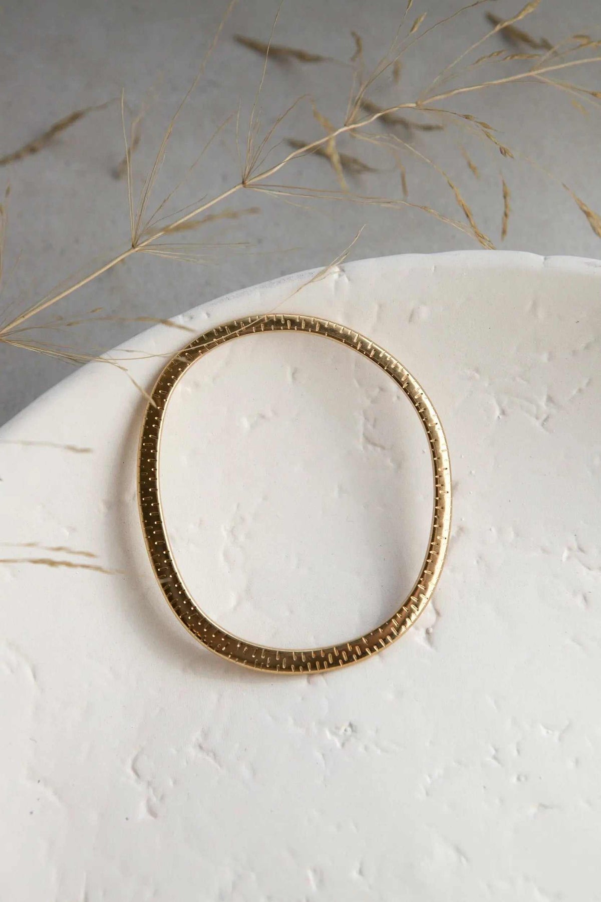 Ethnic Oval bangle in gold-tone metal, slim oval shape with a textured border and fine engraved details