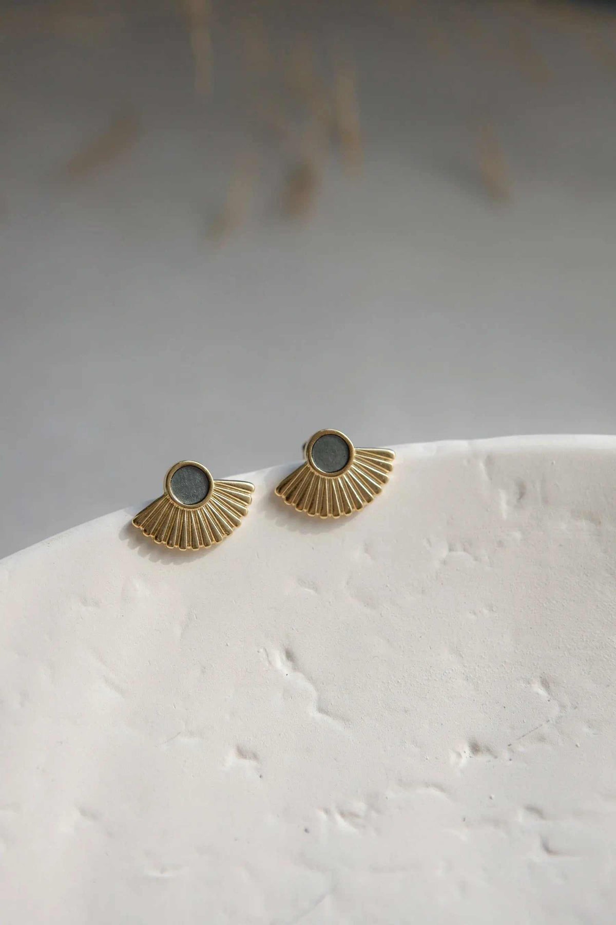 Ethnic stud earrings in gold-toned metal with grey round resin centers and fan-shaped radiating ridges