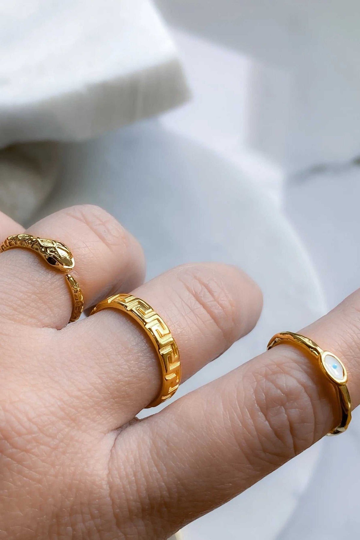 EYE Evil eye ring set of gold-tone bands on fingers, featuring Greek key patterns and small blue-and-white eye details