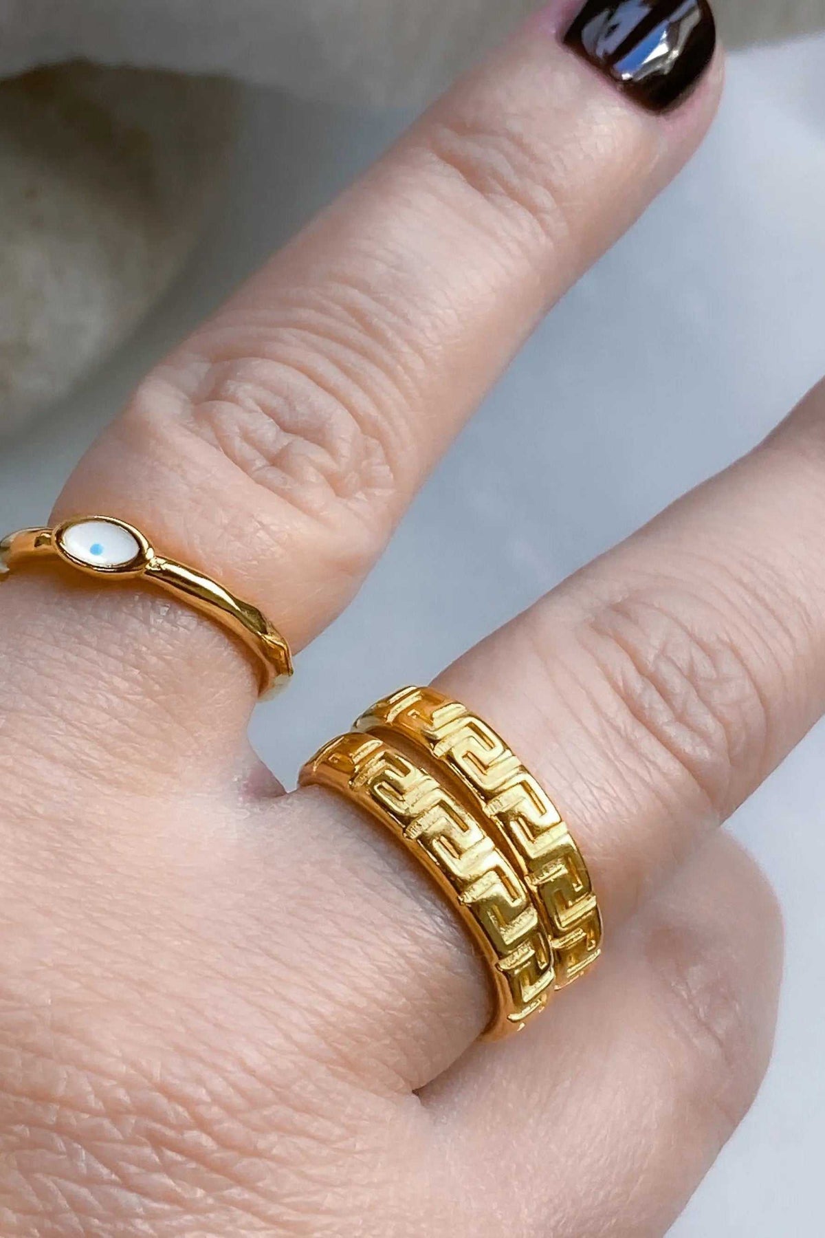 EYE Evil eye ring in gold-tone metal with a slim band and small white oval eye detail, beside a wide patterned ring.