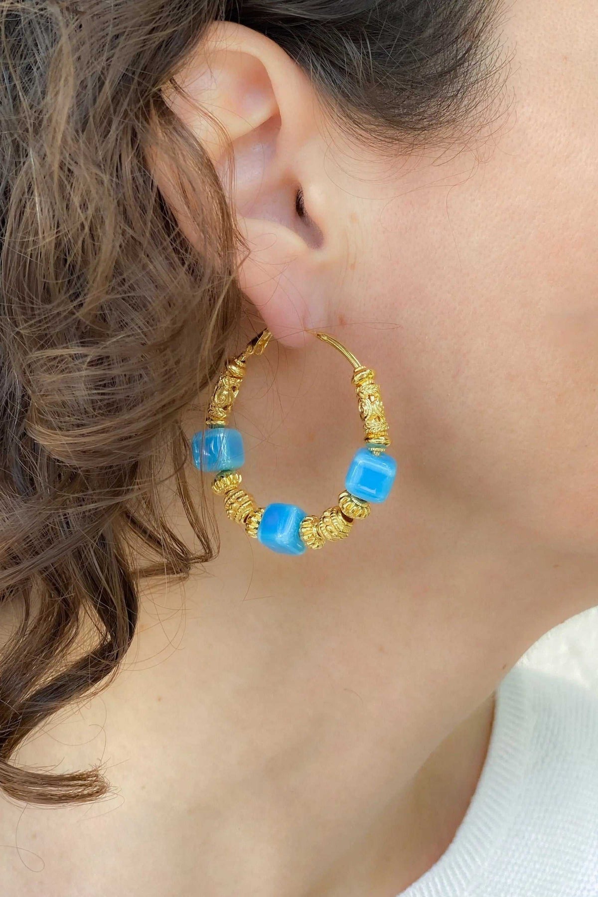 GÉA EARRINGS are gold-tone hoop earrings with bright blue ceramic cube beads and textured coiled details
