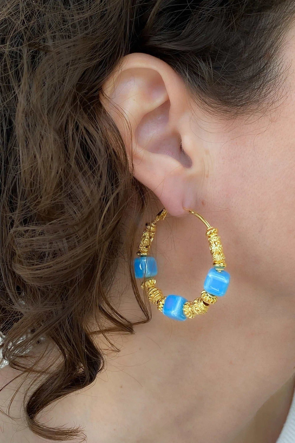 GÉA EARRINGS are gold-tone hoop earrings with bright blue ceramic cubes and ornate textured accents.