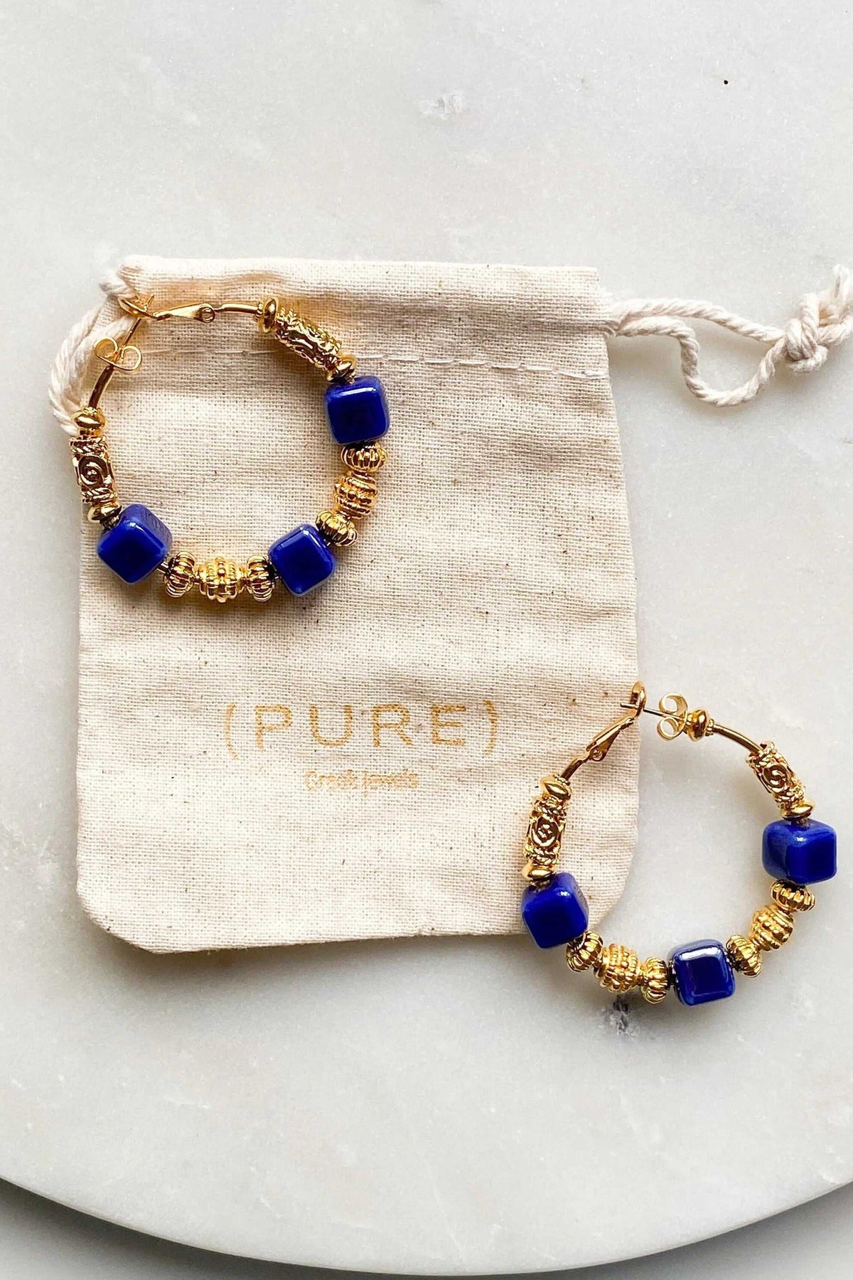 GÉA EARRINGS are gold-tone hoop earrings with vivid blue ceramic cube beads and decorative coiled wire details