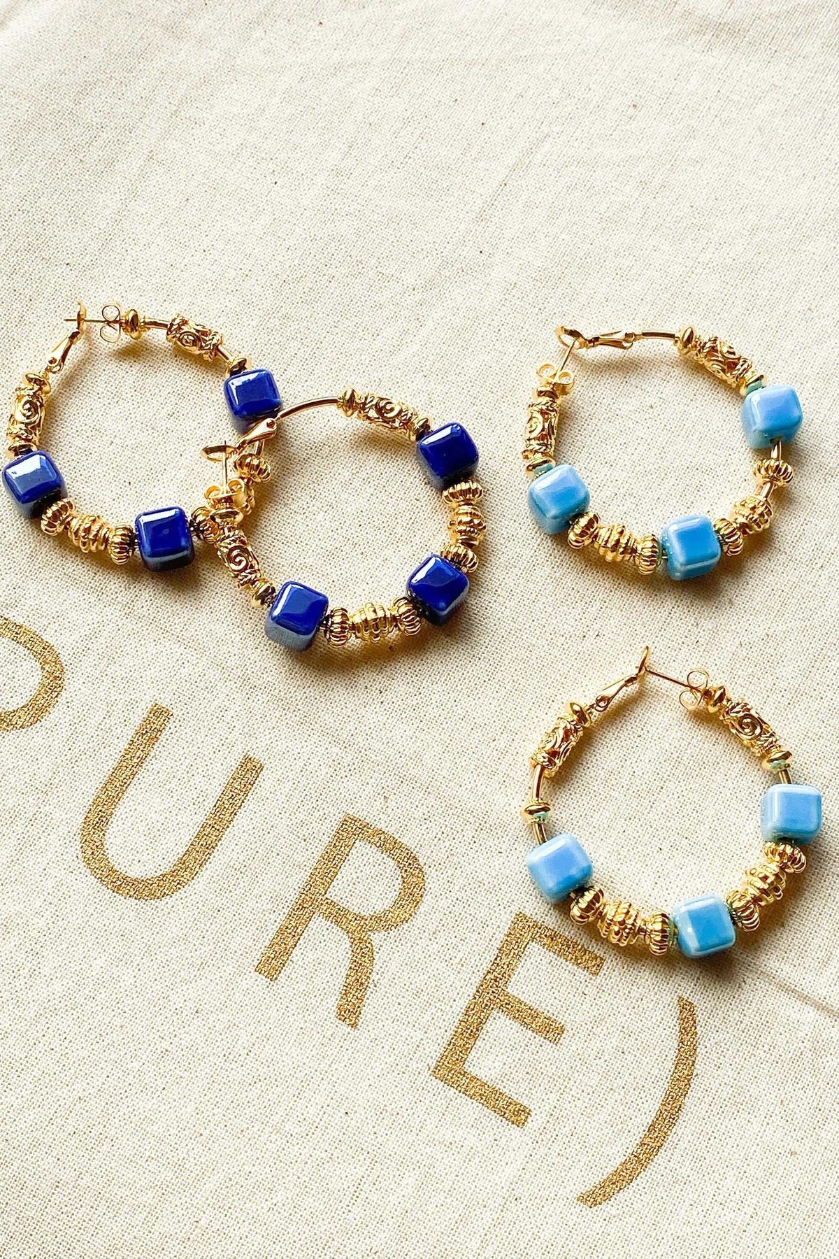 GÉA EARRINGS are gold-tone hoop earrings wrapped with wire and decorated with glossy dark blue and light blue ceramic cubes