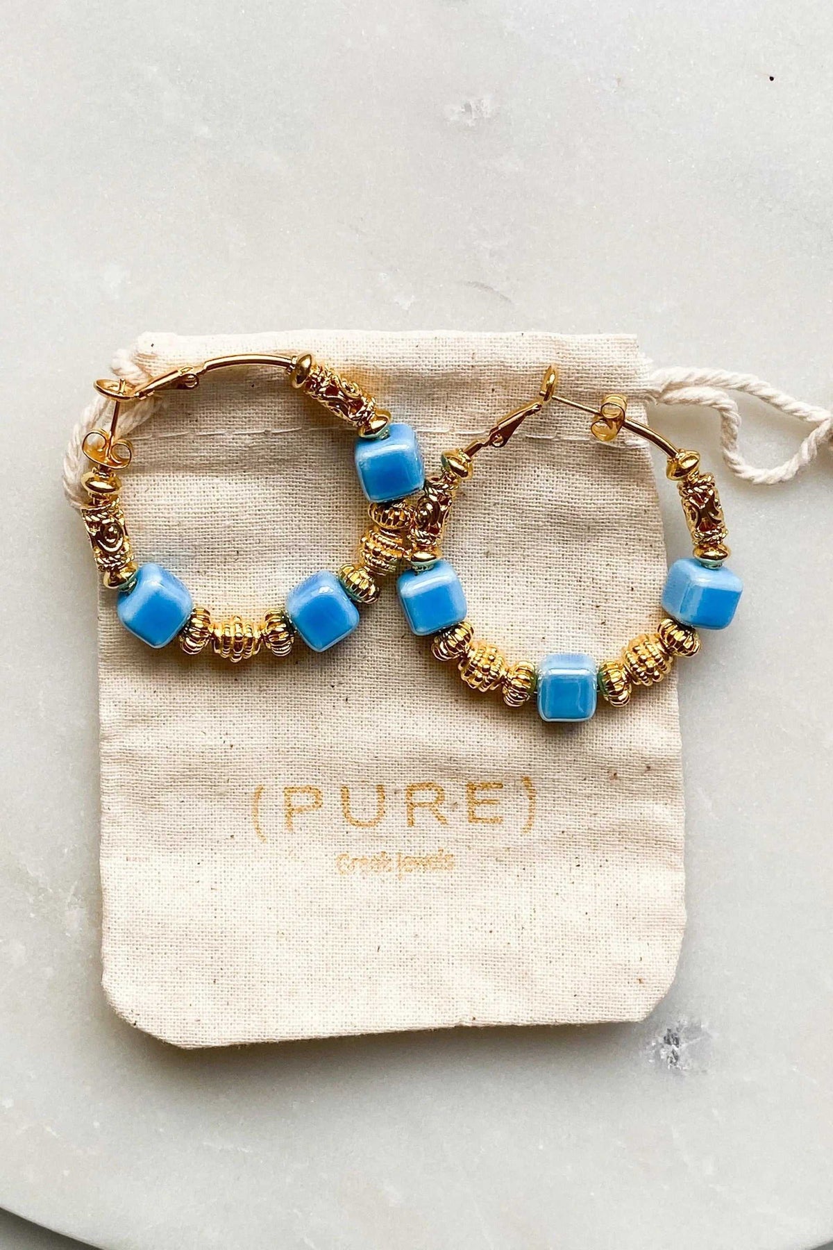 GÉA EARRINGS feature gold-tone hoops adorned with glossy blue ceramic cubes and intricate gold-plated details