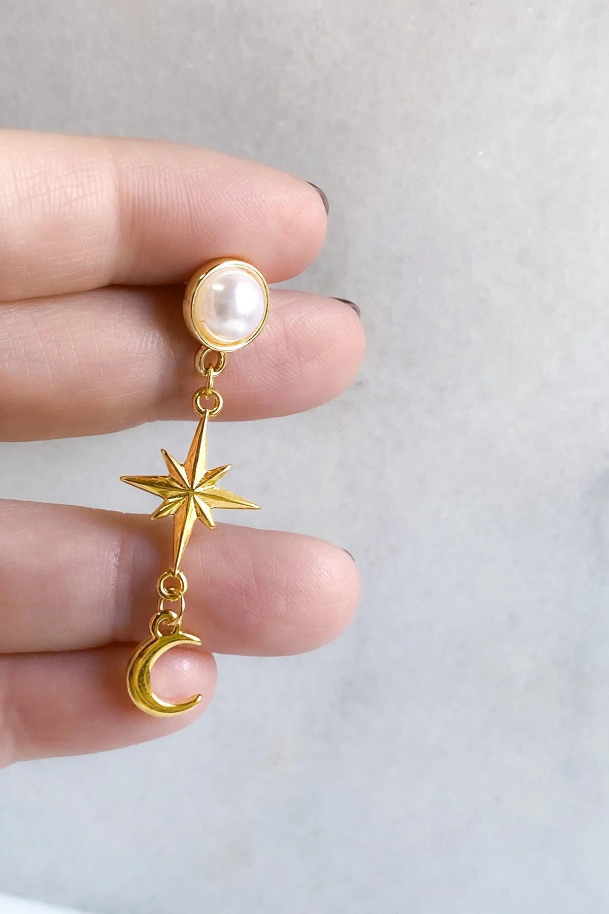 Gold celestial Earrings with a white pearl stud and dangling gold-tone star and crescent moon charms