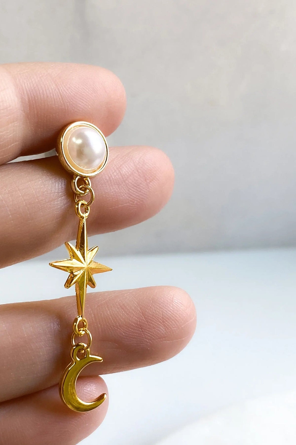 Gold celestial Earrings with a white pearl stud, dangling gold star and crescent moon charms, and polished gold finish