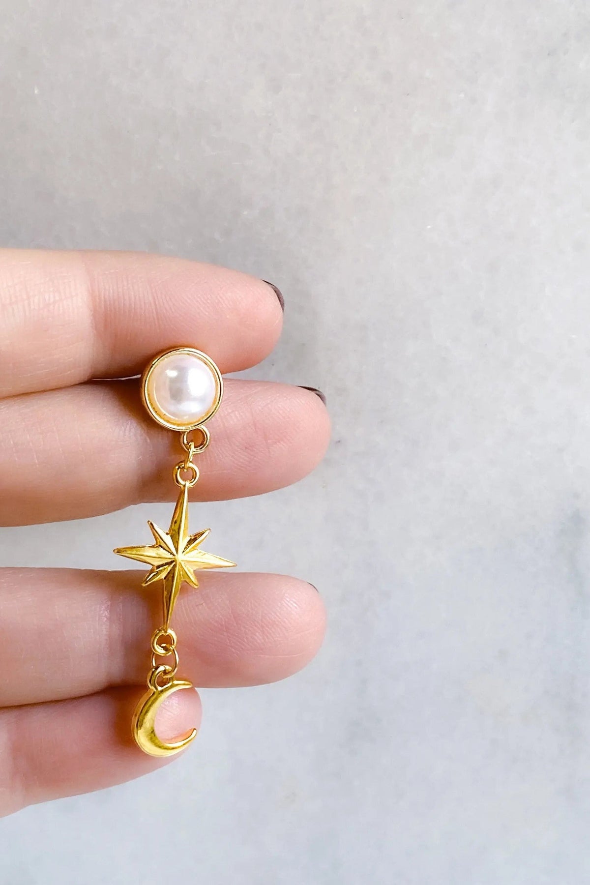 Gold celestial Earrings with a pearl stud, dangling gold star and crescent moon charms, and a pale pink accent