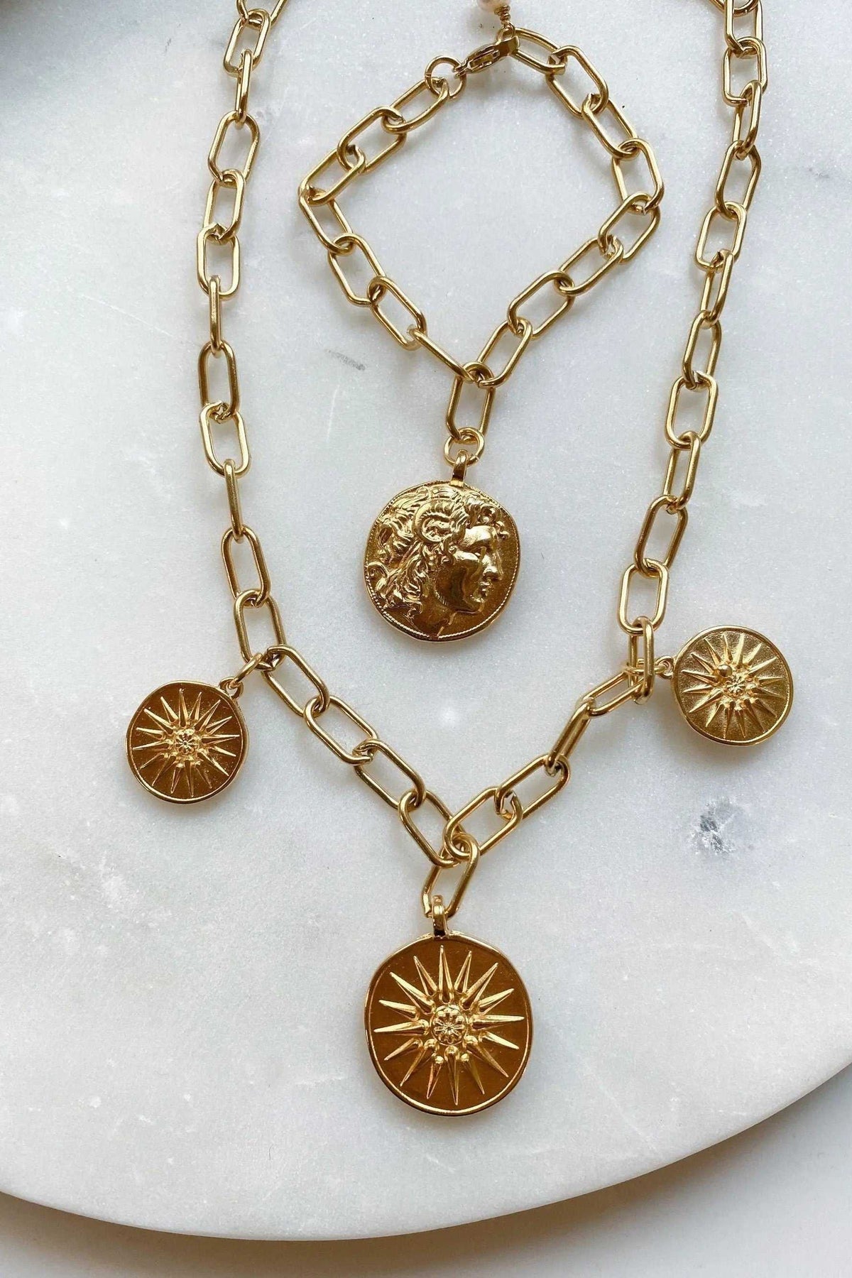 Gold Coin Necklace with shiny gold paperclip chain and round coin pendants featuring raised classical faces and starburst designs
