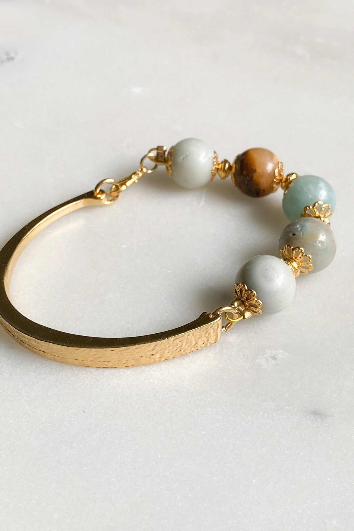 Gold cuff bracelet with a curved gold-tone metal band and round multicolored amazonite beads with gold accents