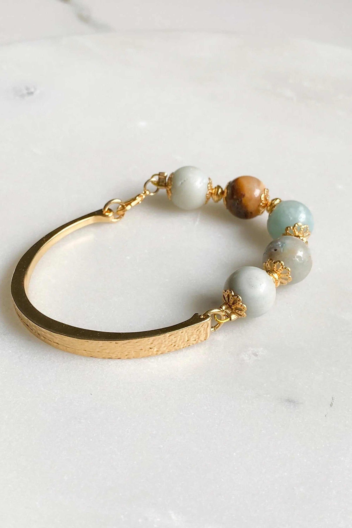 Gold cuff bracelet with a smooth gold-tone metal band and pale blue, white, and brown beads with ornate gold spacers