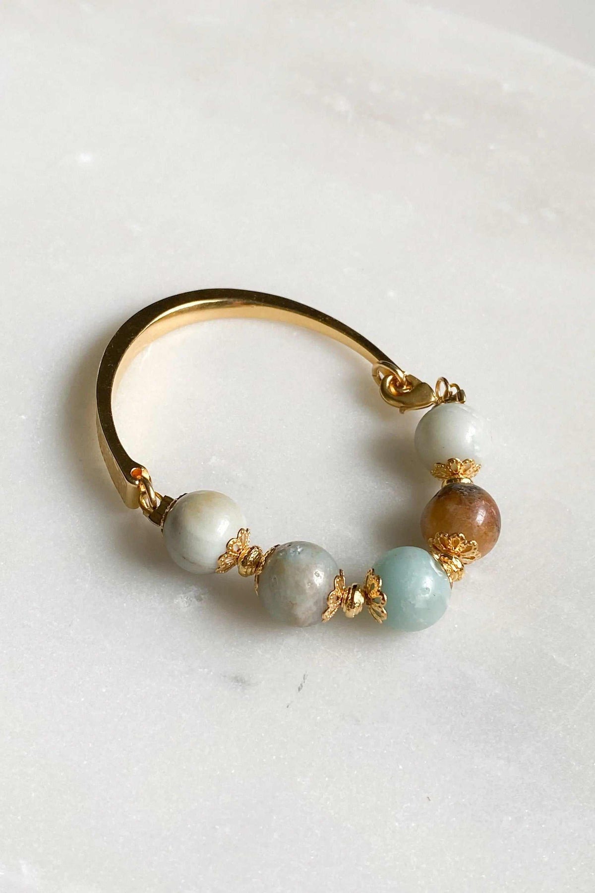 Gold cuff bracelet with a polished gold-tone open band and pale blue, white, and brown round beads with gold accents