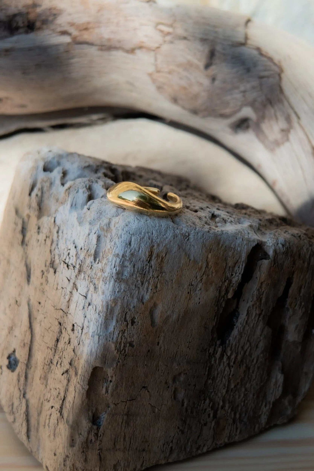 Gold dome ring in a polished gold tone, featuring a sculptural, asymmetrical wave-shaped band with a raised curved detail.