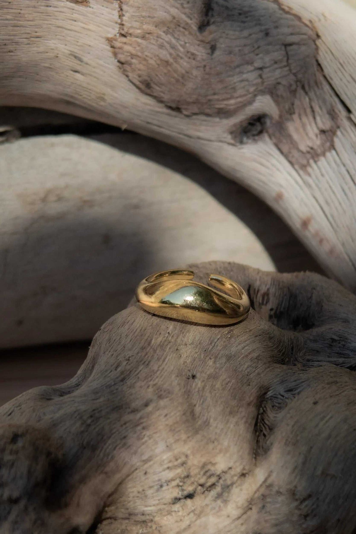 Gold dome ring in polished gold-tone metal, featuring a wide, rounded band with a sculptural wave-like shape