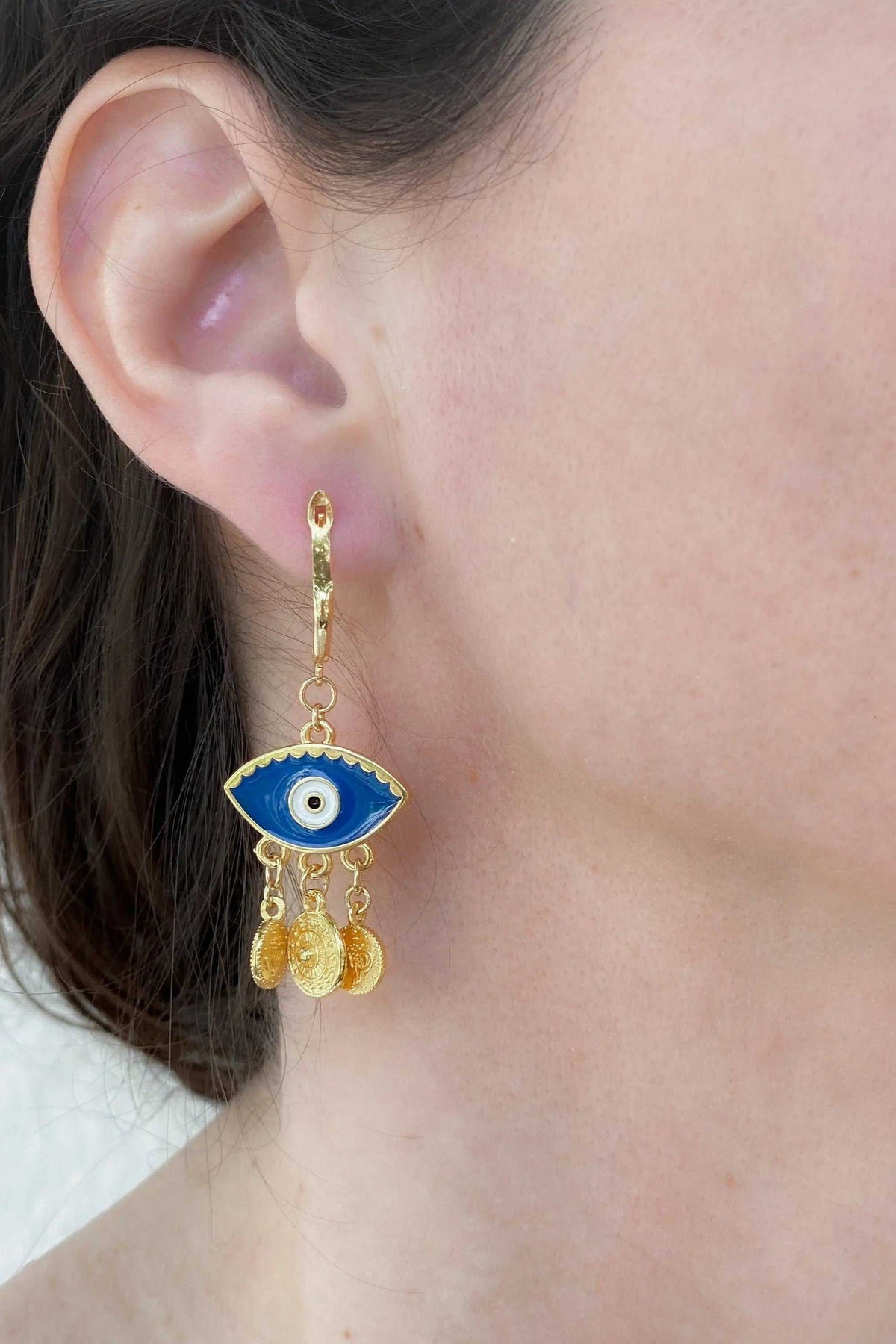 Gold evil eye earrings with blue enamel eye motif, dangling gold charms, and slender drop design