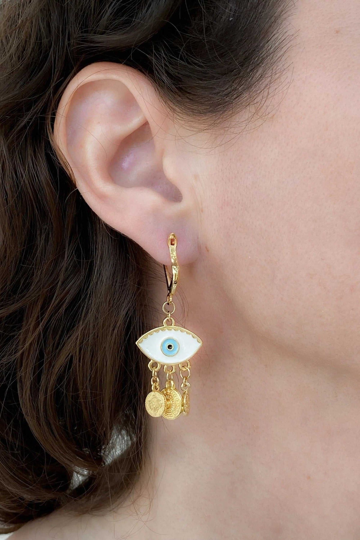 Gold evil eye earrings with polished gold-tone hooks, white enamel eye charms, and dangling gold discs.