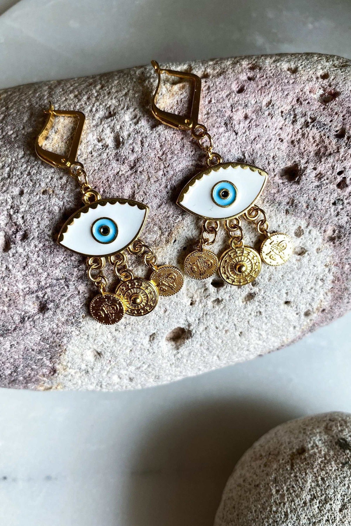 Gold evil eye earrings with white enamel eye motifs, blue centers, and dangling gold-tone coin charms