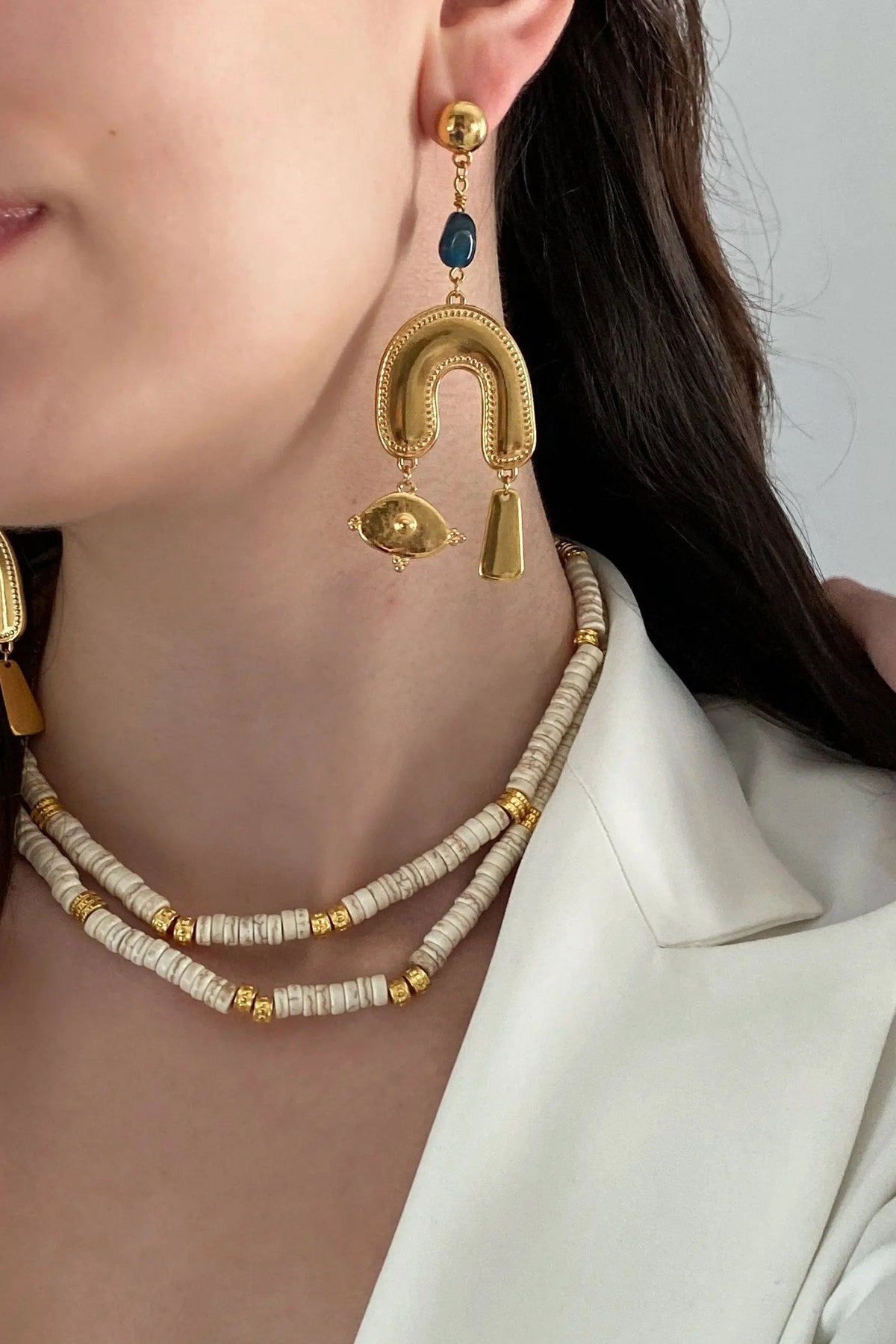 Gold Gypsy Earrings with a blue oval bead, textured U-shaped gold centerpiece, and dangling eye and bar charms.