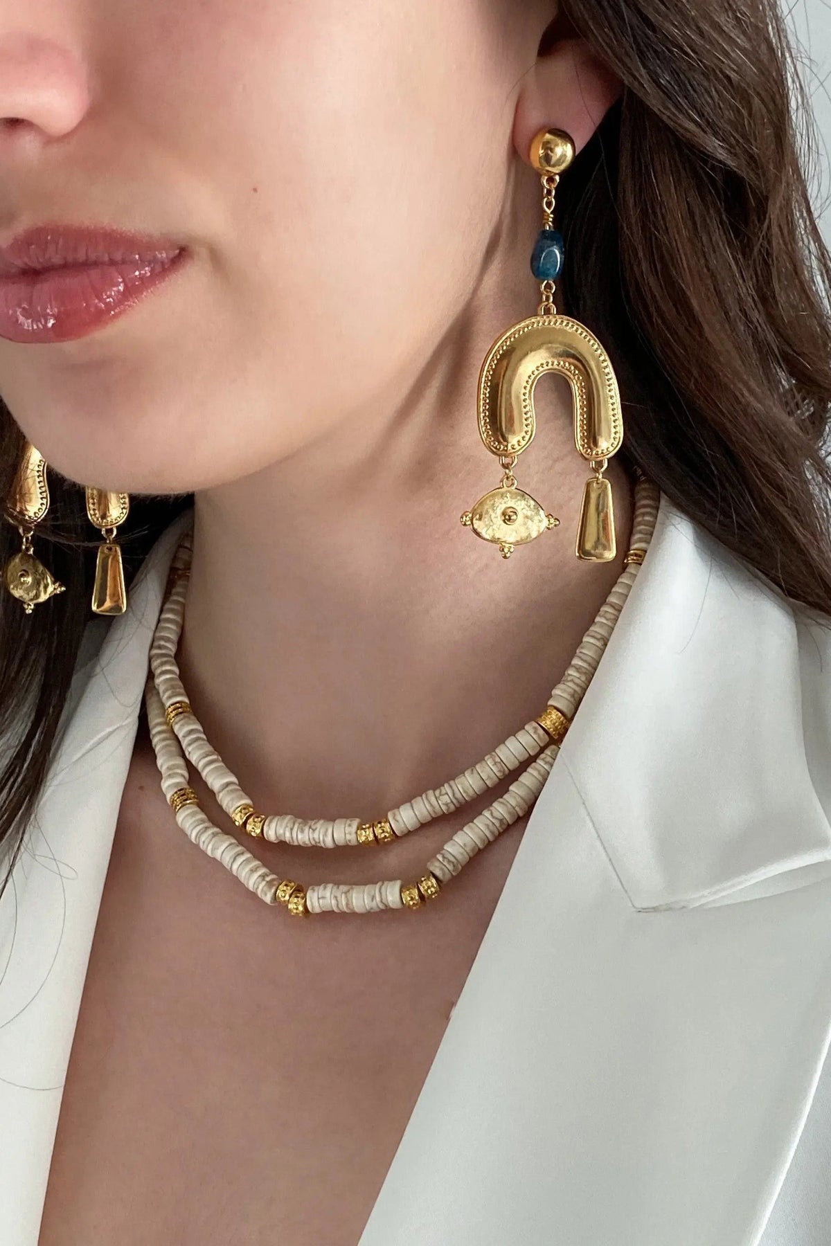 Gold Gypsy Earrings with blue beads and ornate gold-tone chandelier charms, worn with layered neutral beaded necklaces