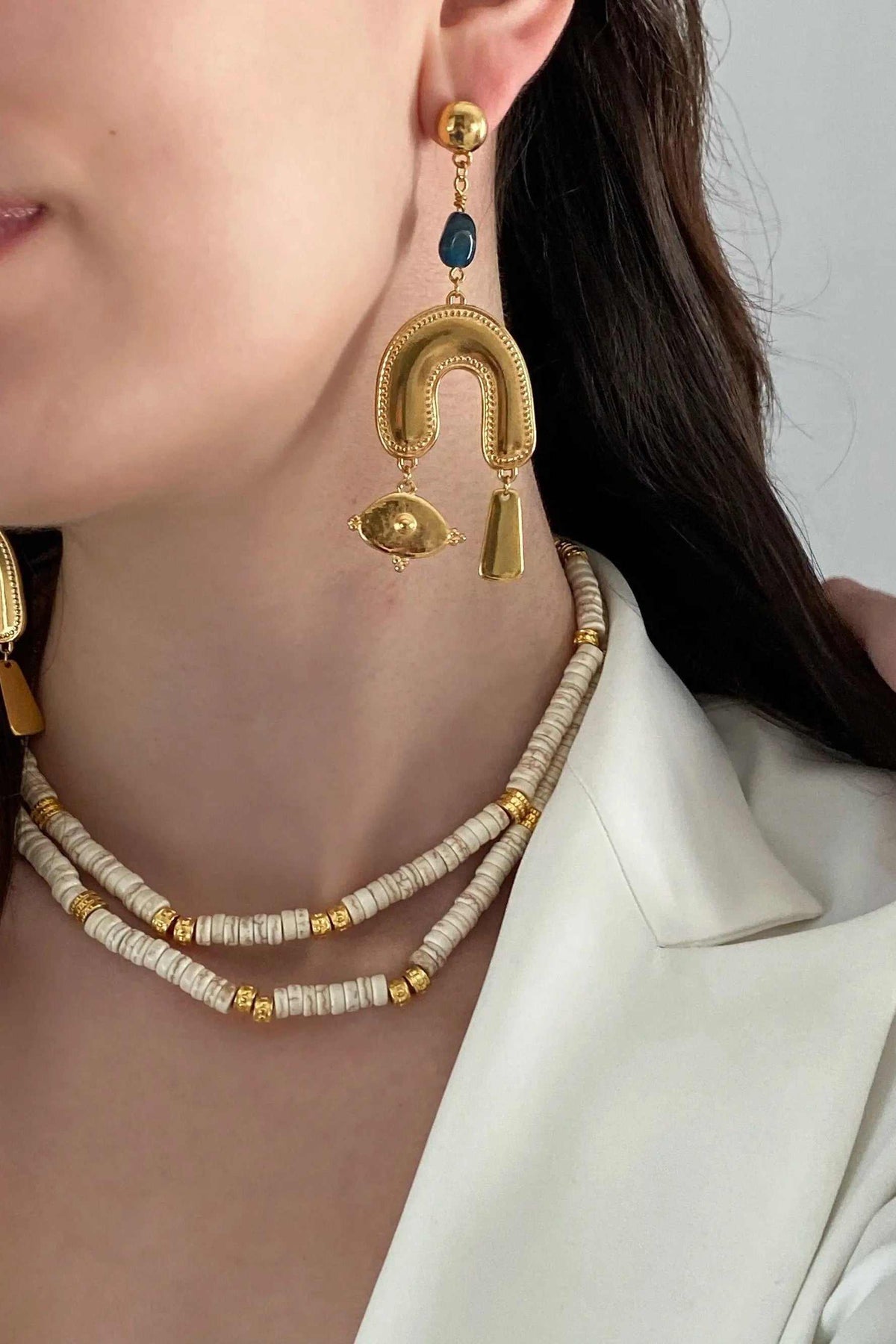 Gold Gypsy Earrings in ornate gold-tone metal with a blue oval stone and dangling eye and bar charms