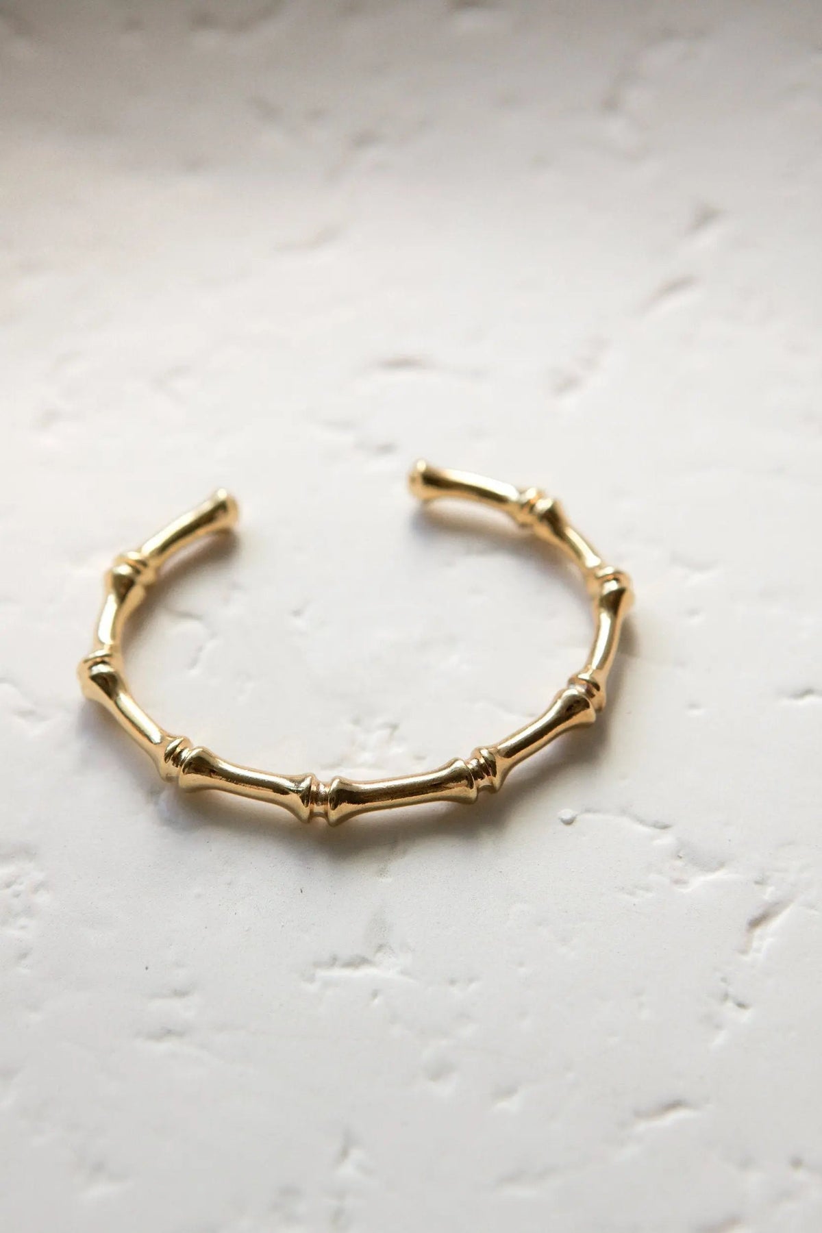 Gold hoop earrings with a polished gold-tone finish, designed as an open cuff with raised bamboo-like segments