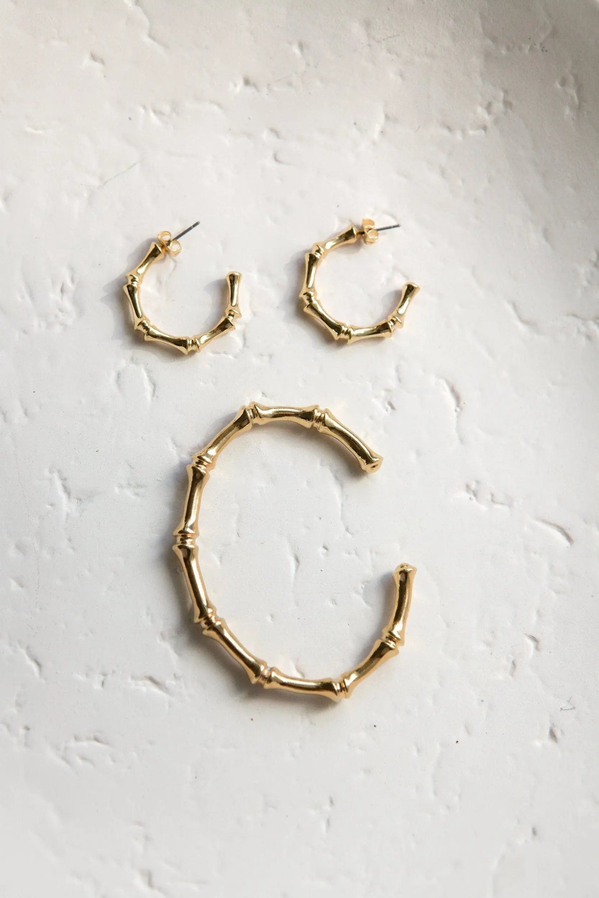 Gold hoop earrings in polished gold-tone metal, with irregular bamboo-inspired segments and hinged clasp closures.