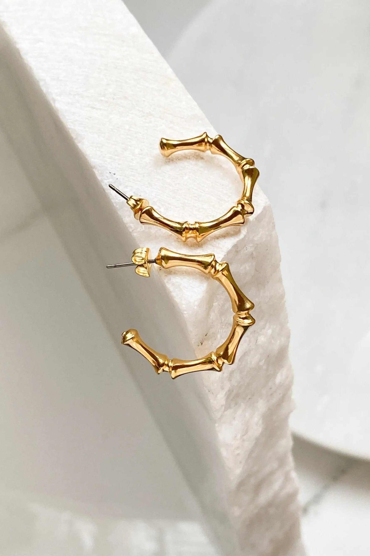 Gold hoop earrings in polished gold-tone metal, shaped with irregular bamboo-like segments and slim posts.