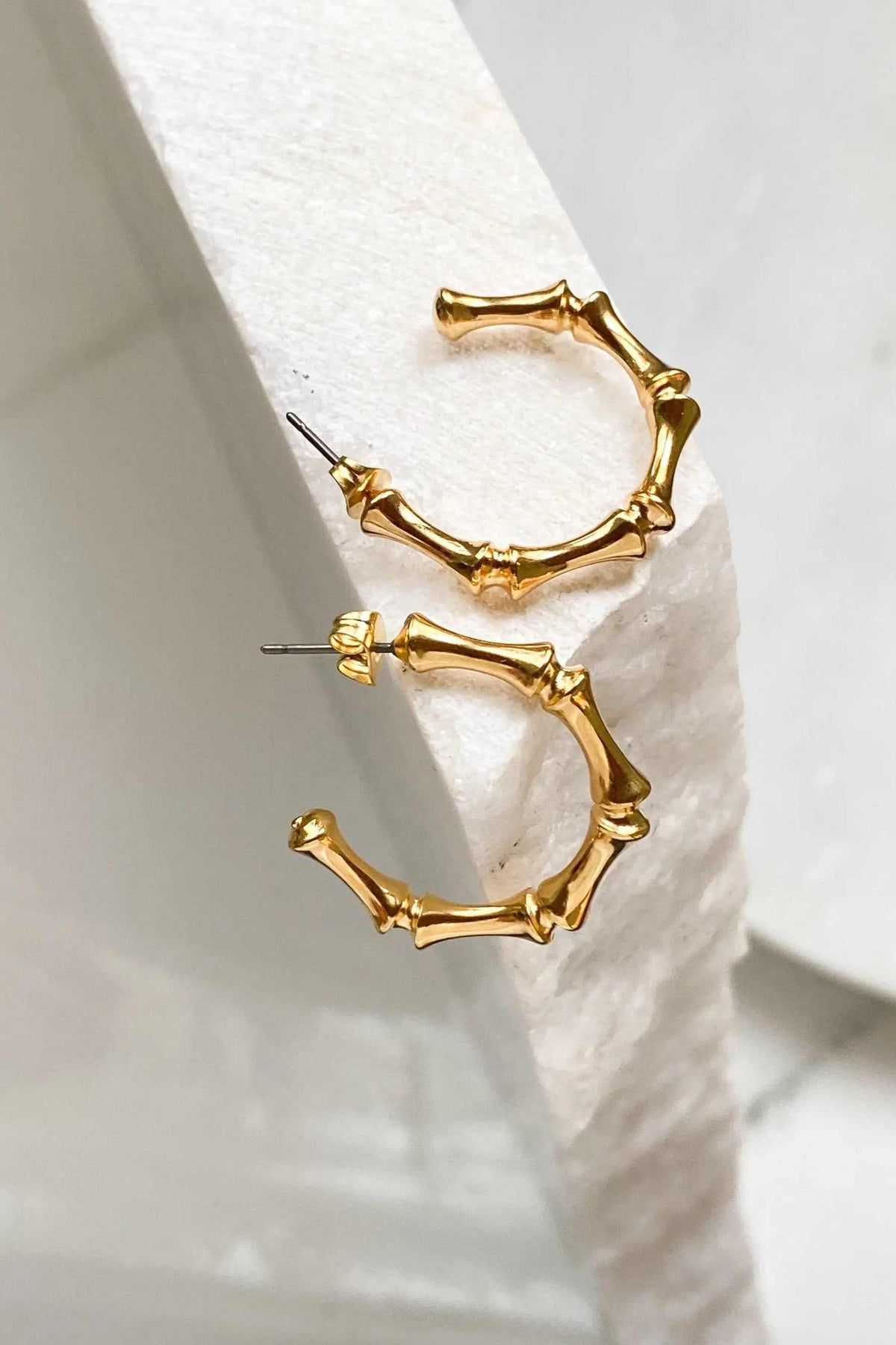 Gold hoop earrings in polished gold-tone metal, featuring sculptural bamboo-like segmented hoops with irregular joints