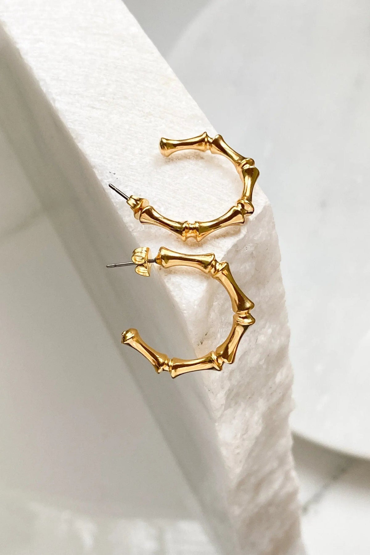 Gold hoop earrings with polished gold-tone bamboo-inspired segments and slim straight posts, forming open circular hoops.