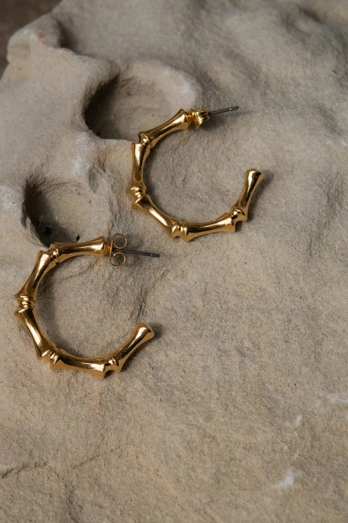 Gold hoop earrings with a polished finish and sculptural bamboo-like segments, featuring titanium pin posts.