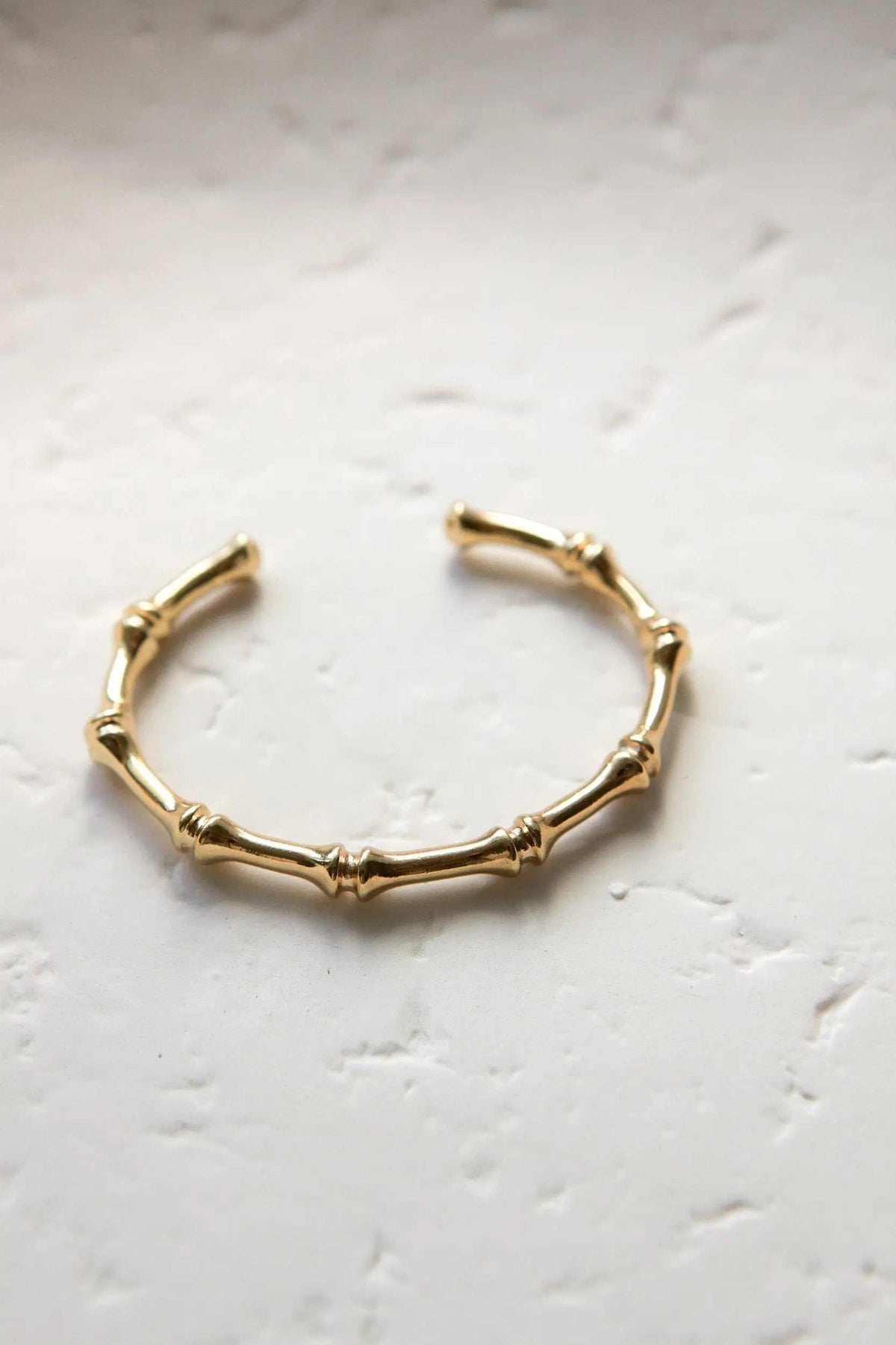 Gold hoop earrings with a polished finish and sculpted bamboo-style segments forming an open circular shape