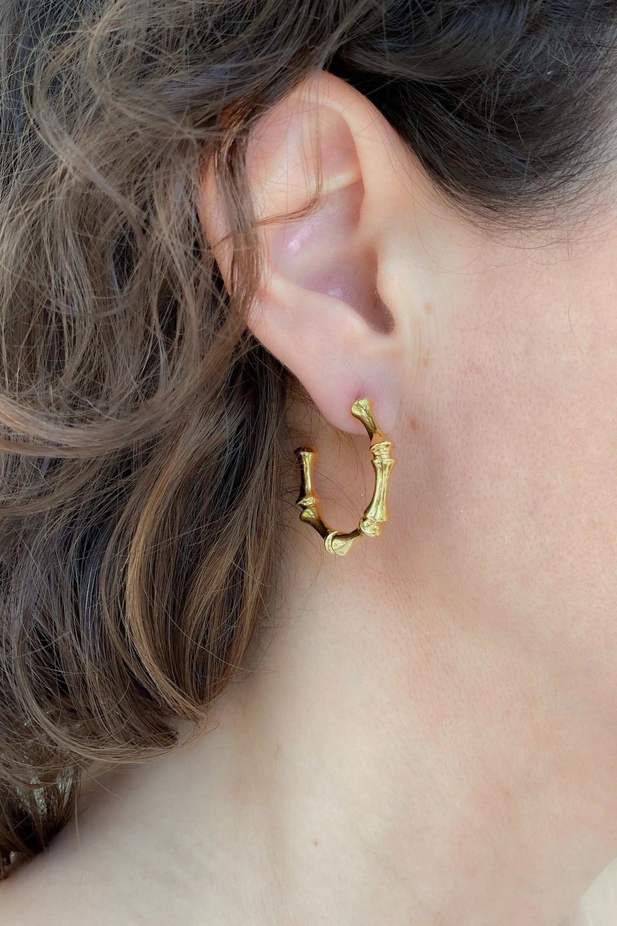 Gold hoop earrings in a bright gold tone with a textured, irregular oval shape and small sculptural details