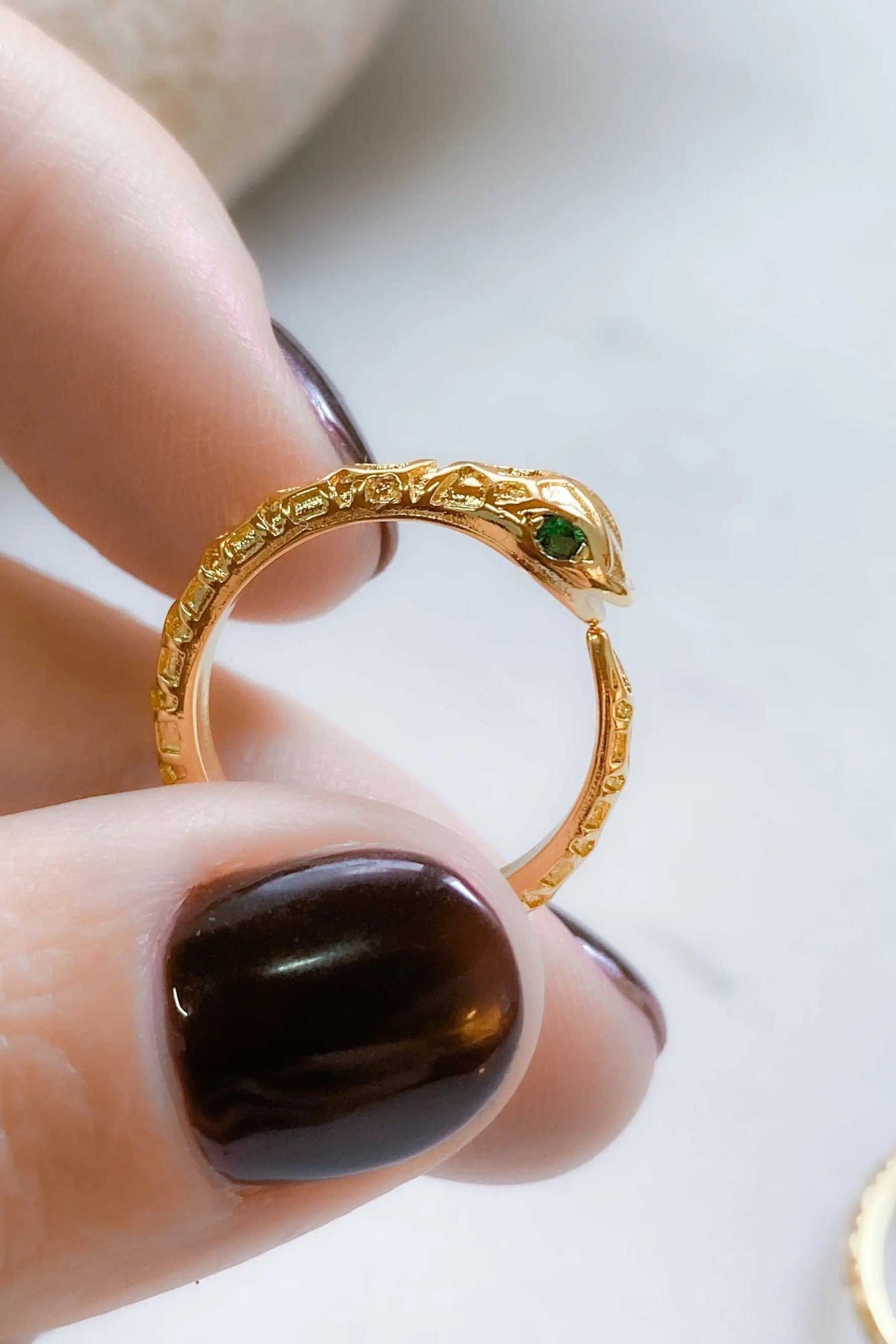 Gold Snake RING with a textured gold-tone serpent design and a small green eye stone, held between fingers