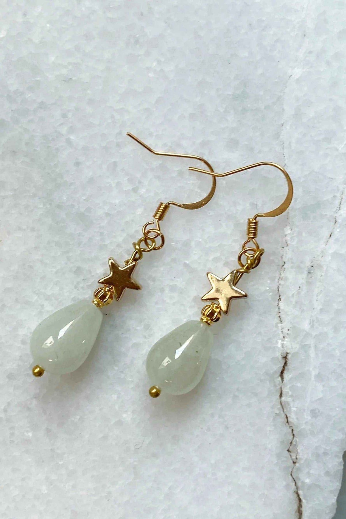 Gold star earrings with gold-toned star charms and pale green teardrop stones on dangling hooks