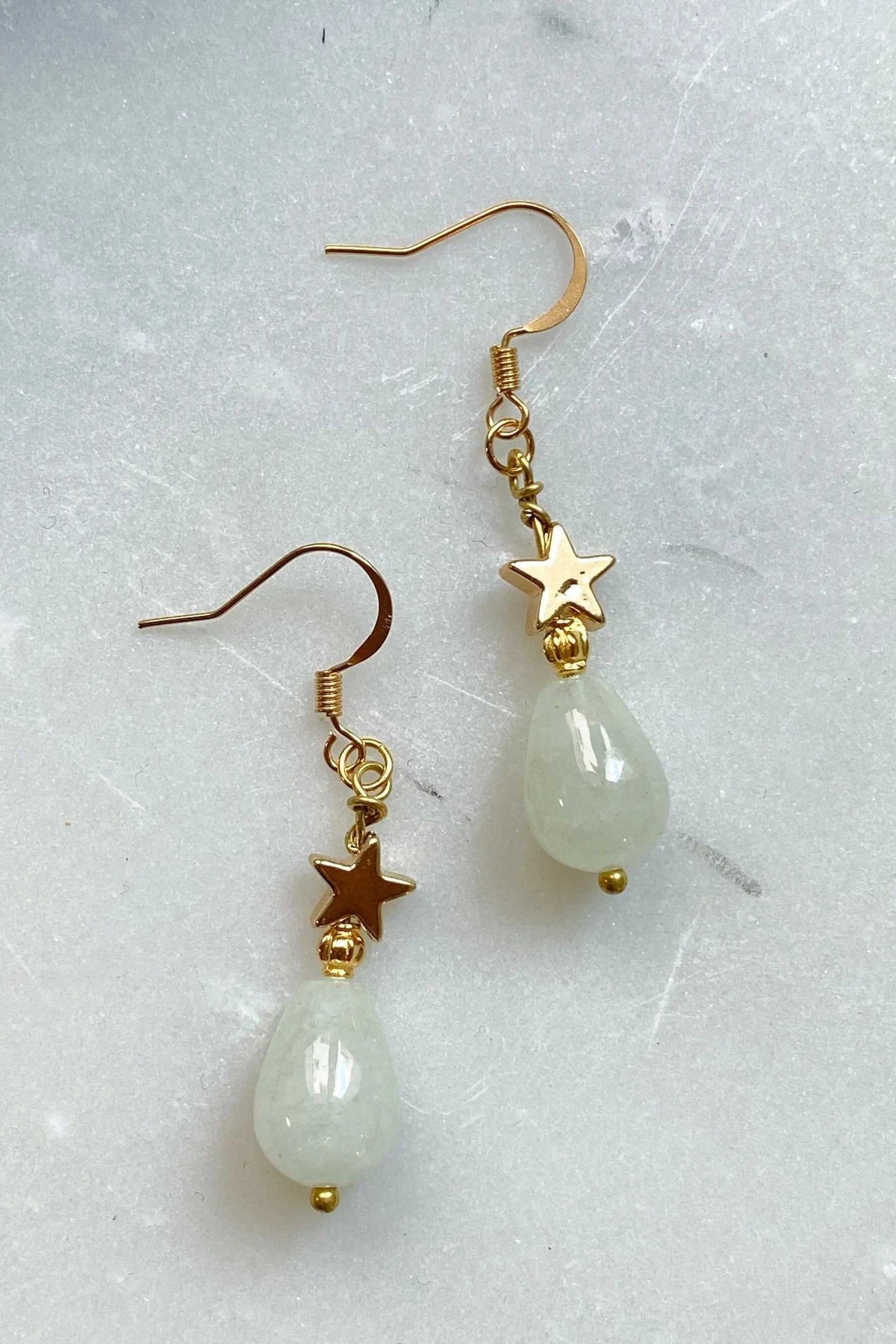 Gold star earrings with pale green teardrop stones, polished gold star charms, and dangling bead details