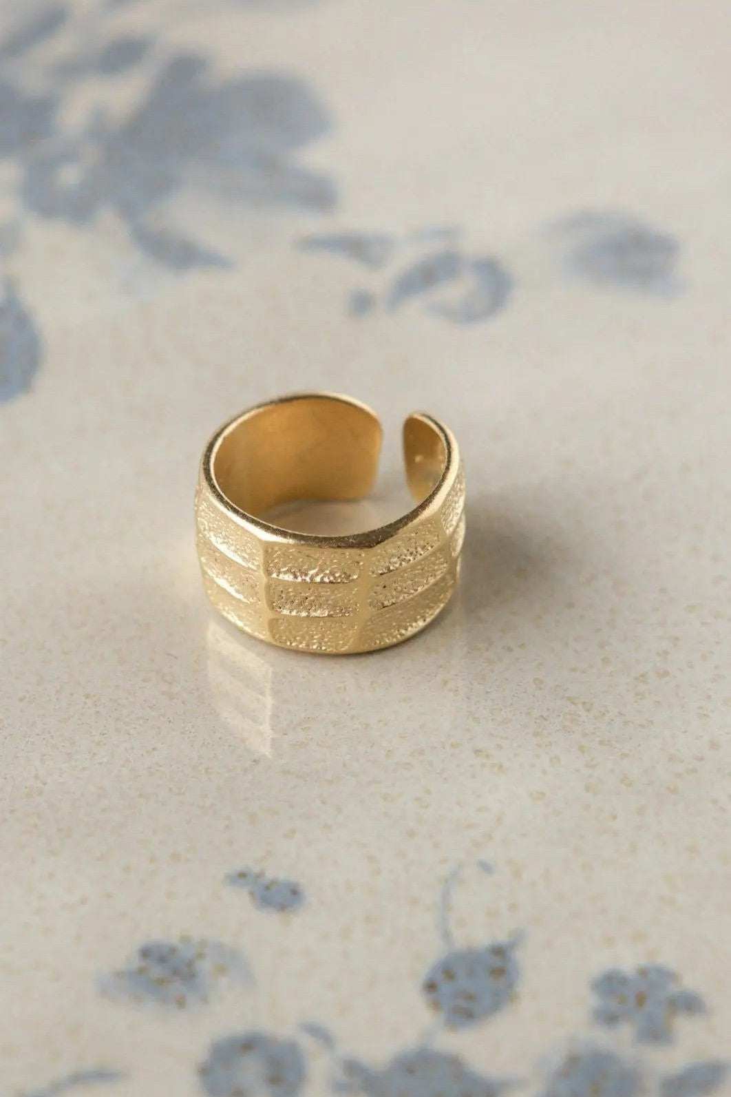 Greek wide ring in gold-tone metal with a broad textured band, raised horizontal lines, and an adjustable open end