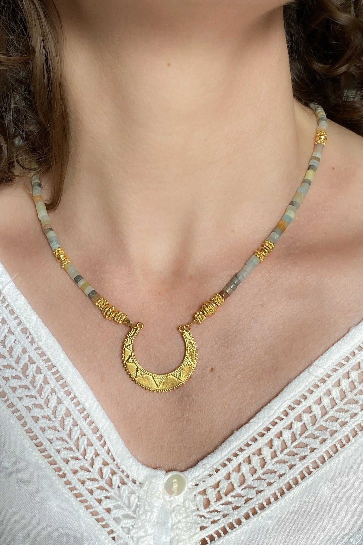 Heishi Necklace with pale blue and beige beads, gold accents, and crescent pendant with engraved motif