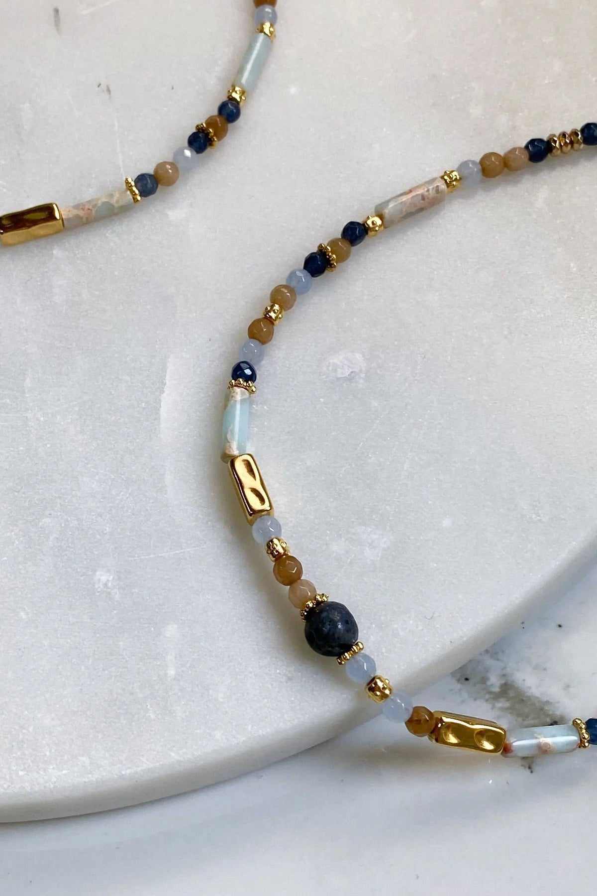 Heishi Necklace with blue and beige stone beads, white cylindrical beads, gold accents, and clasp details