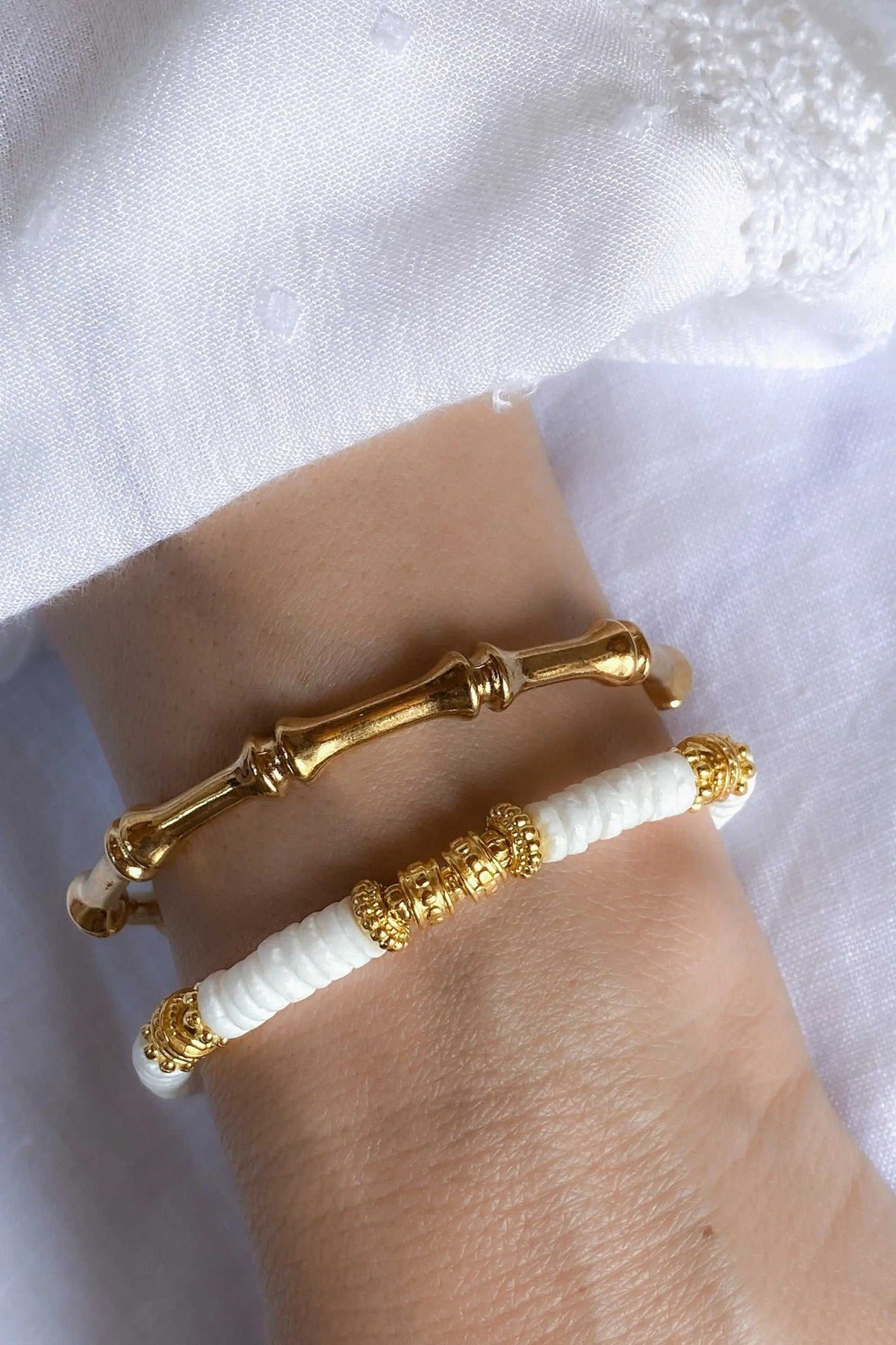 Bracelet with white Heishi shell beads, gold-tone ornate spacer beads and a polished gold bar clasp on the wrist
