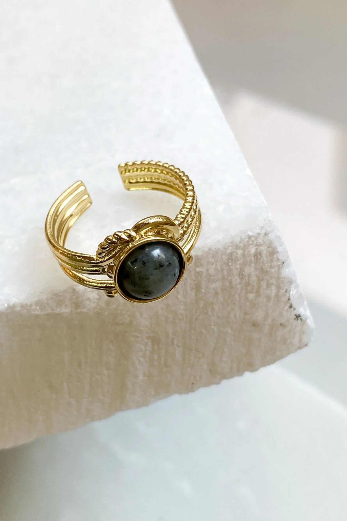HERMINA Gold Stone Ring with a dark grey oval stone and ornate gold-tone open band with ridged details