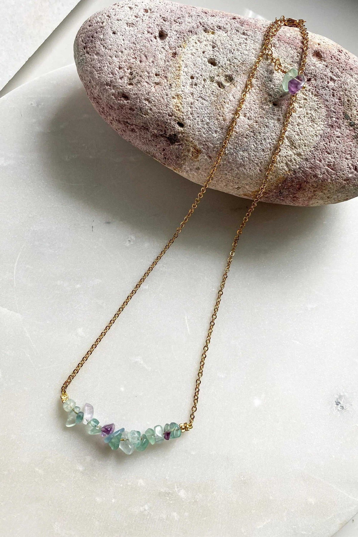 Hoop crystal earrings are not visible; image shows a fine gold-tone necklace with pale green and purple gemstone chips.