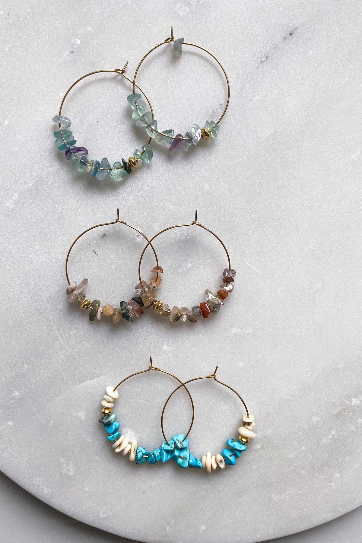 Hoop crystal earrings with thin gold-tone hoops and clusters of irregular translucent green, earthy brown, and turquoise stones