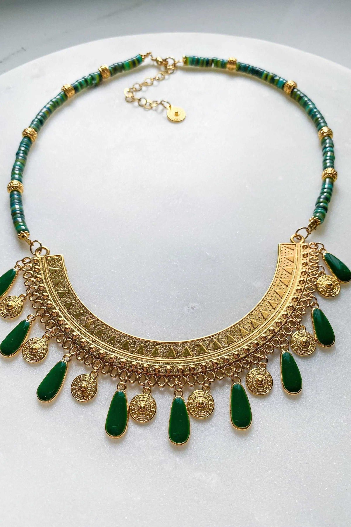 ILIADA NECKLACE with green beads and an ornate gold-tone geometric pendant, finished with dangling green teardrops and coin charms