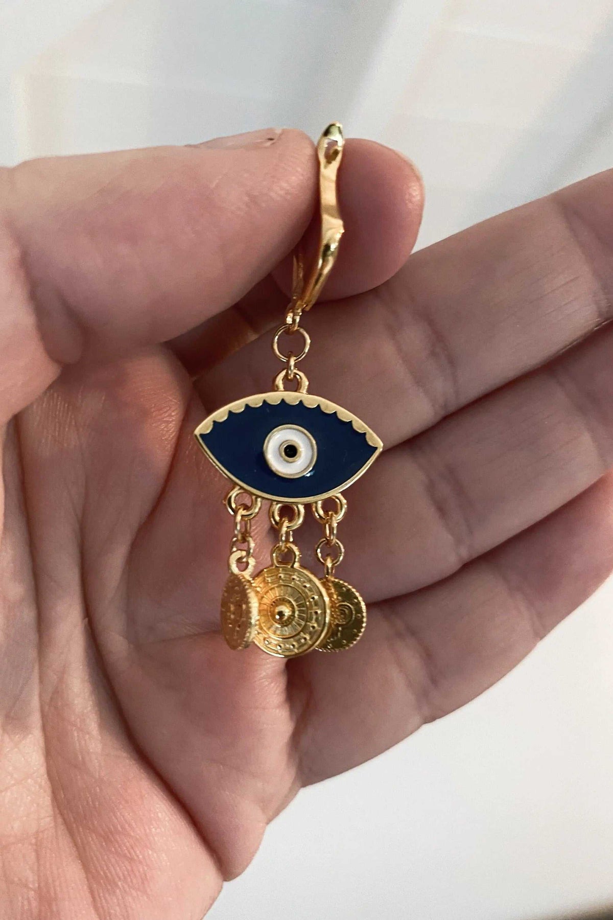 IOLI EARRINGS are gold-tone brass drops with a dark blue enamel eye motif and dangling coin charms