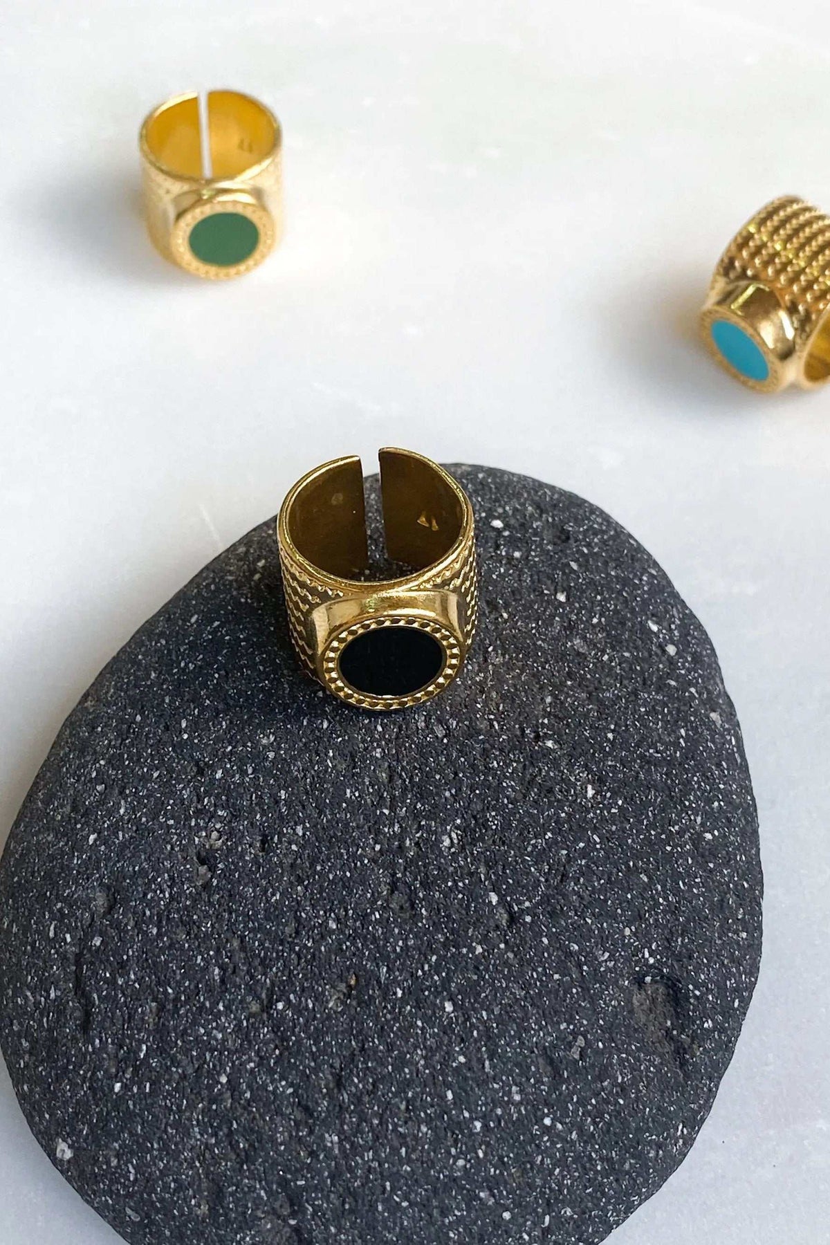 KARMI Gold wide band ring in gold-tone metal, with a black oval resin stone and an adjustable open band