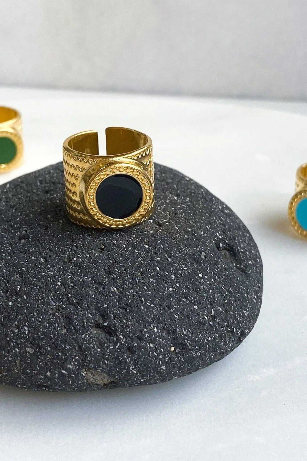 KARMI Gold wide band ring in textured gold-tone metal with a round black resin stone and open adjustable band