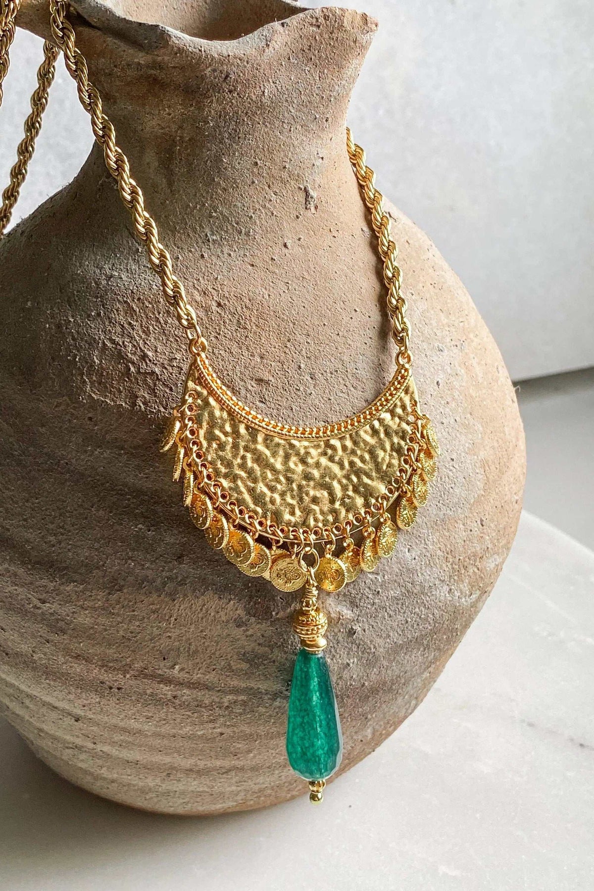 KIVÉLI Boho Necklace in gold-tone metal with hammered pendant, coin details, and green teardrop gemstone